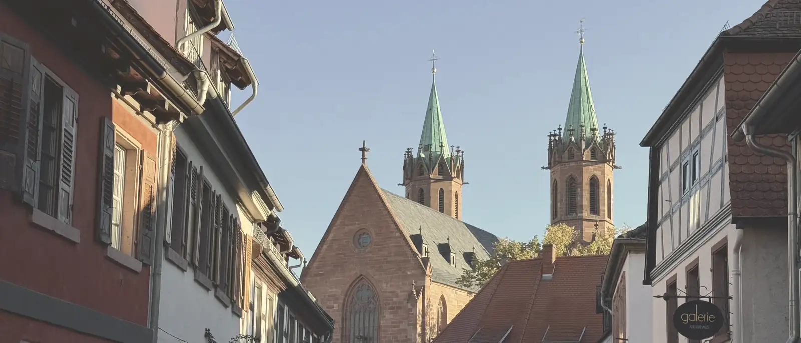 Blick durch eine Gasse der Ladenburger Altstadt auf die Kirche St. Gallus mit ihren zwei Türmen