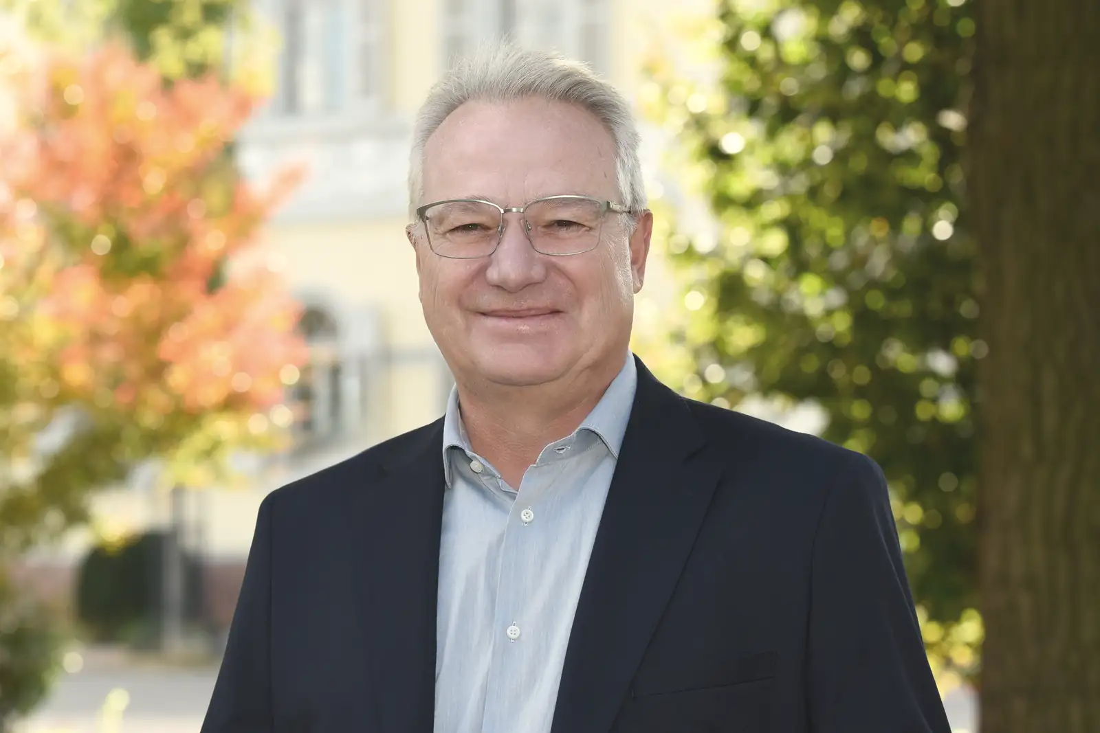 Rechtsanwalt Klaus Kalinski im Park, hinter ihm eine helle Villa und herbstliche Bäume