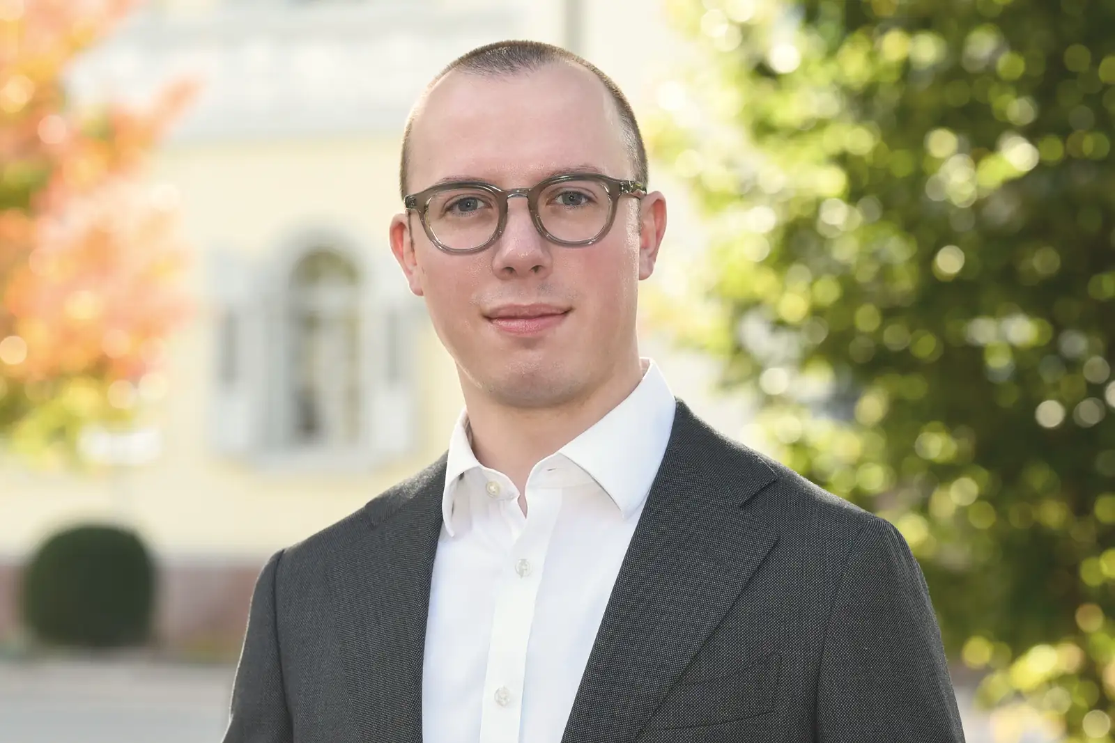 Rechtsanwalt Tom Kalinski im Park, hinter ihm eine helle Villa und herbstliche Bäume